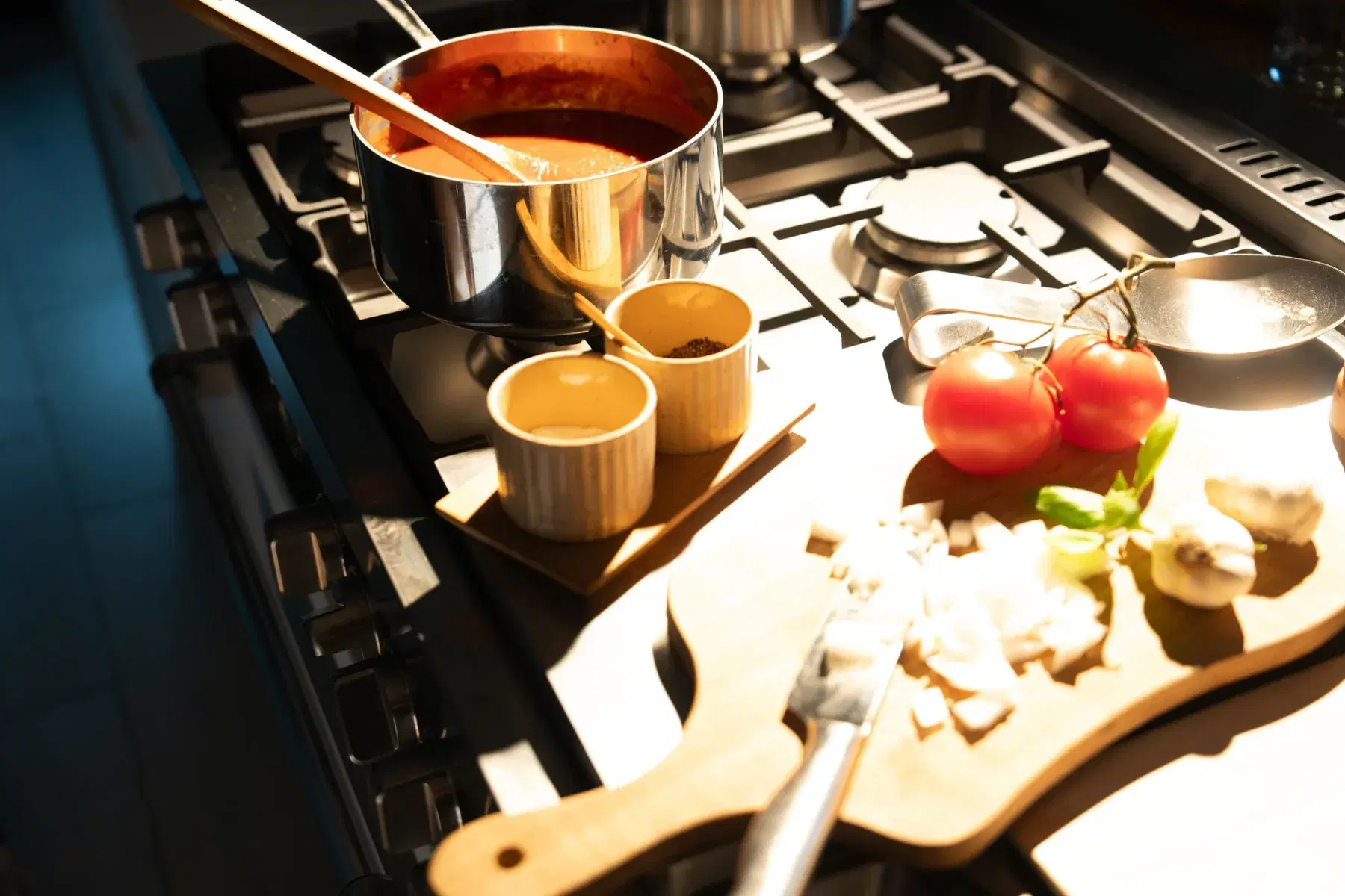 Tomato sauce simmering on a stove beside spice cups and a board of chopped onion