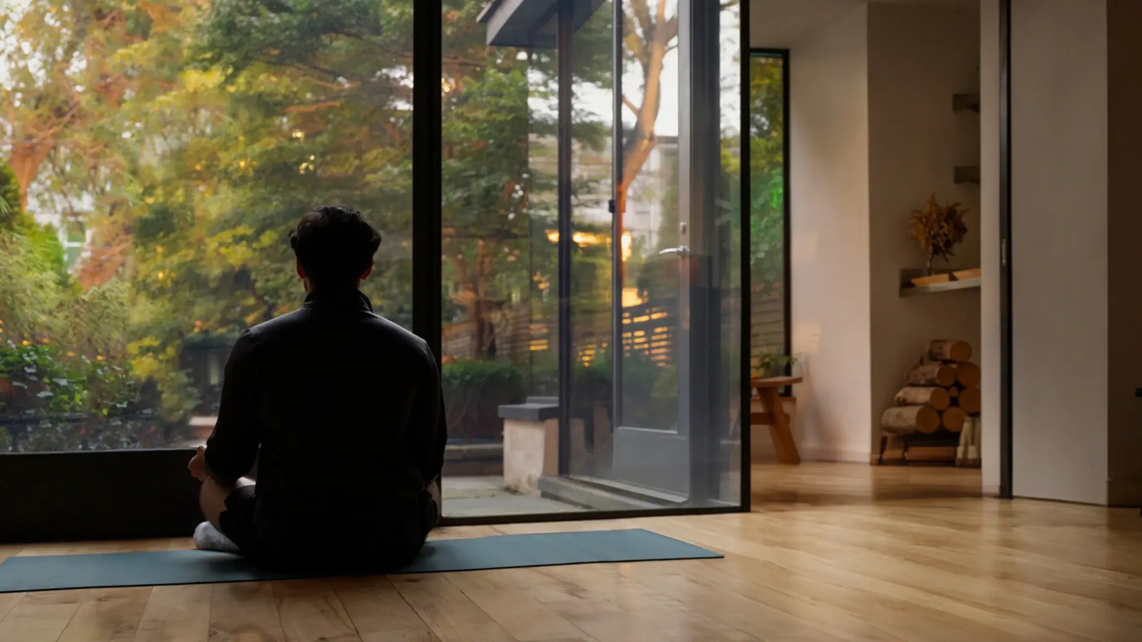 A person meditating by a floor-to-ceiling window at dusk