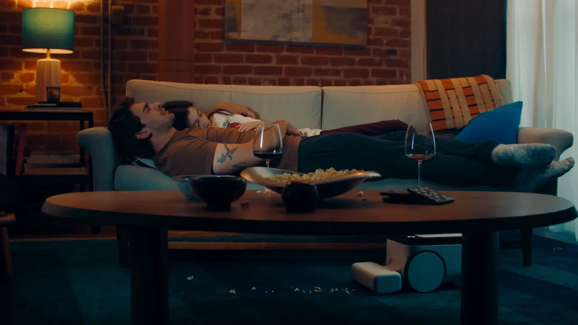 A couple asleep on the sofa while Matic quietly cleans popcorn from under the coffee table
